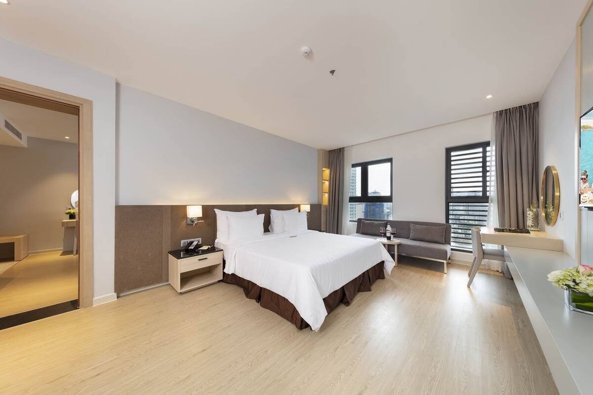 A modern hotel room with a large bed, a seating area, and a view of the city.
