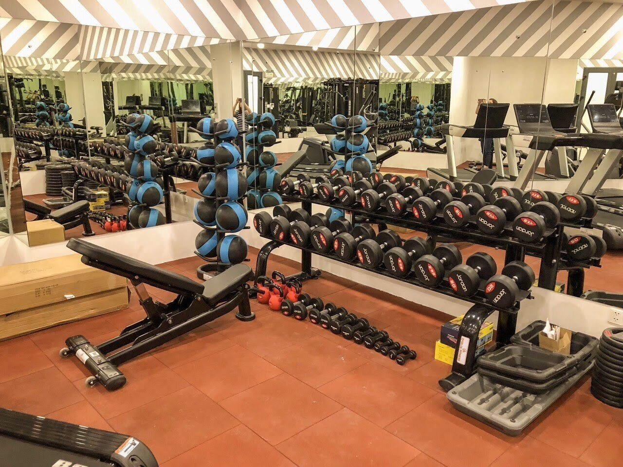 Ein Fitnessraum mit verschiedenen Trainingsgeräten, darunter Kurzhanteln, Kettlebells und Kraftmaschinen.