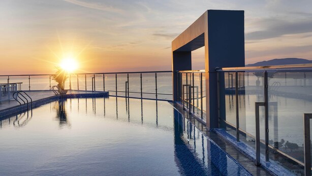 A modern infinity pool with a glass railing, reflecting the sunset over a body of water. - DQua Hotel (Nha Trang)