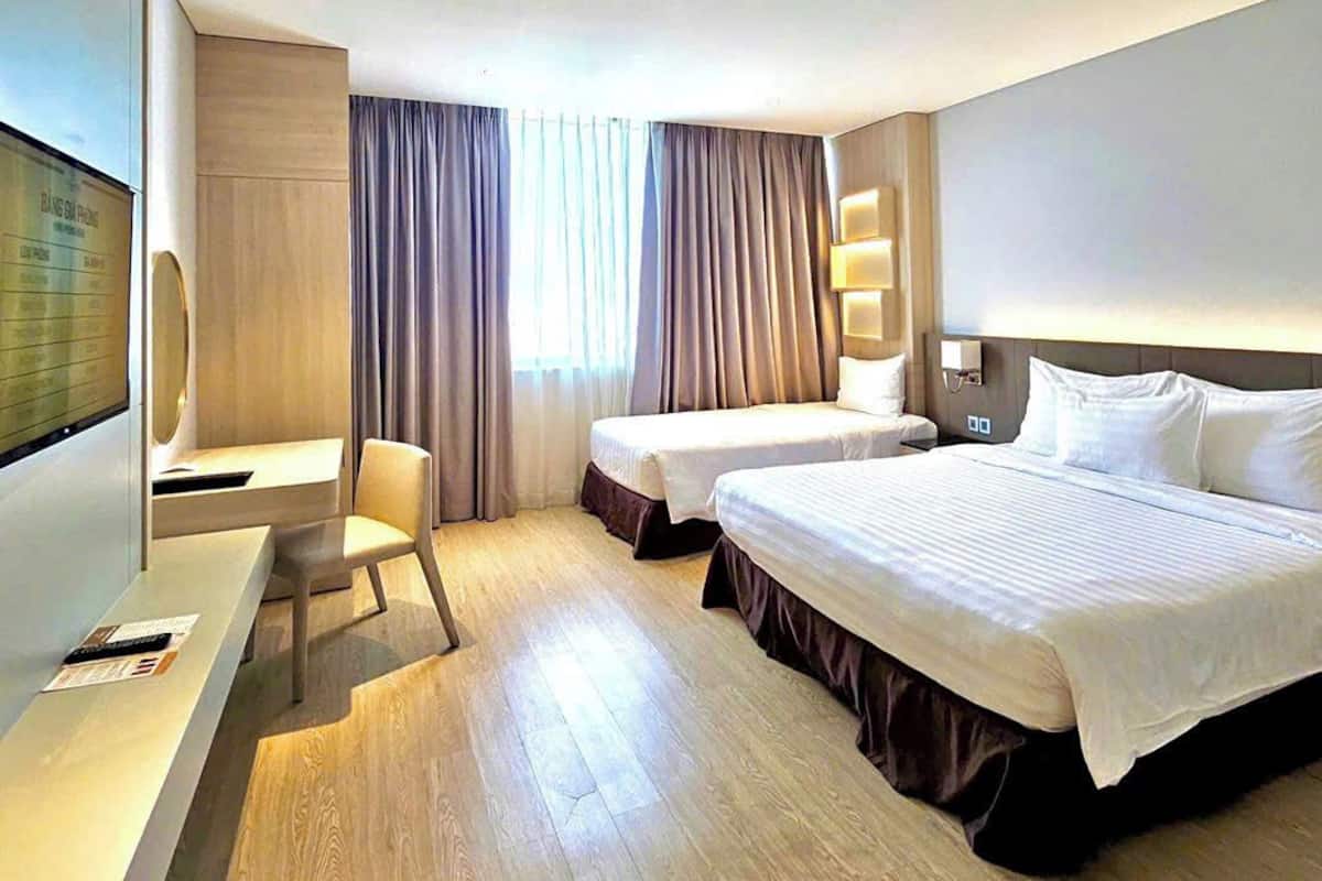 A hotel room with two beds, a desk with a chair, a TV, and a large window with curtains.