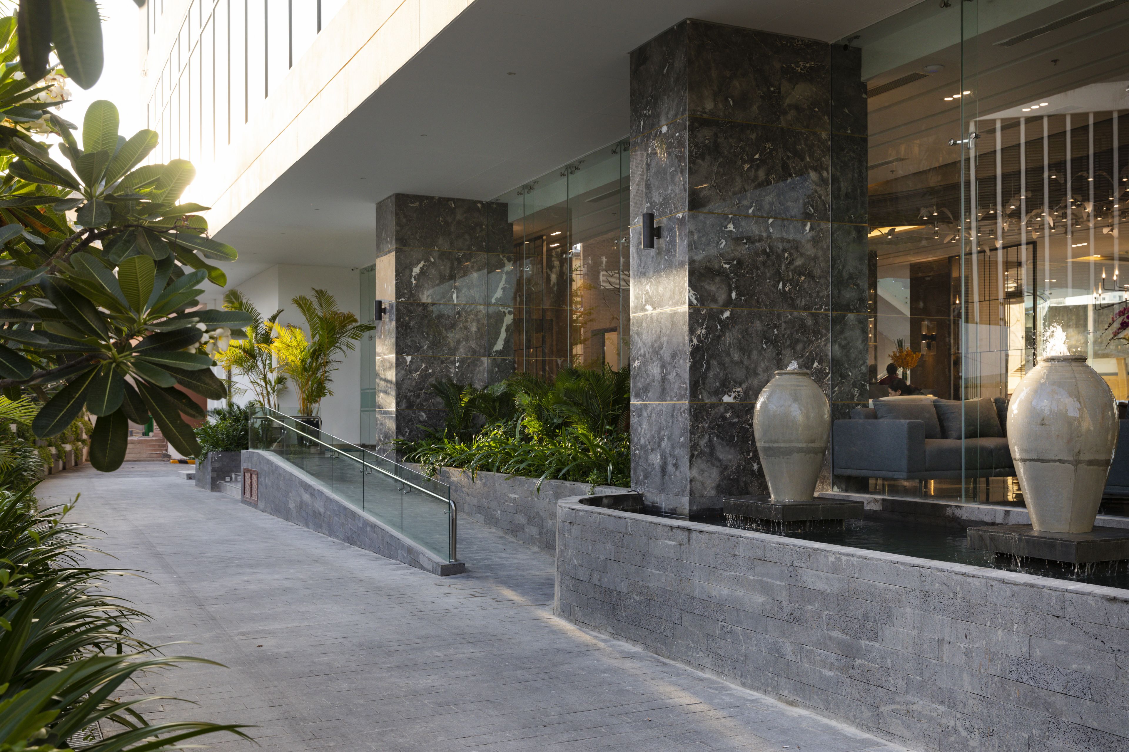 Un moderno vestíbulo de hotel con mostrador de recepción de mármol, una escalera de cristal y plantas de interior.