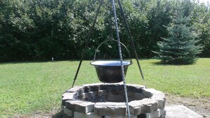 A circular stone fire pit with a metal pot suspended above it. - Apartman Daniel (Balatonfokajár)