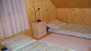 A small, wooden-paneled room with two single beds, a nightstand, and a window with curtains. - Apartman Daniel (Balatonfokajár)
