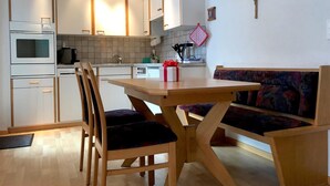 A modern kitchen with white cabinets, a wooden dining table, and a bench with a patterned cushion. - Apartment Azurit by Interhome (Saas-Fee)