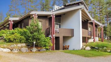 Eine zweistöckige Holzhütte mit geneigtem Dach und einer Veranda mit Stühlen.
