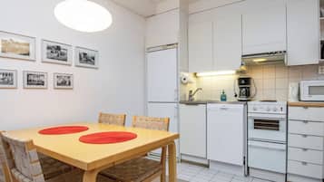 Eine kleine Küche mit weißen Schränken, einem Holztisch mit roten Tischsets und einer hängenden Lampenleuchte.