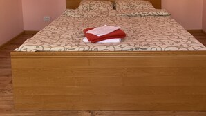 Cama bem arrumada com colcha estampada e duas almofadas, cabeceira de madeira e mesa de cabeceira pequena com abajur.