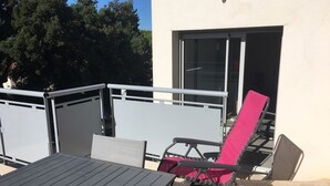 Une terrasse extérieure avec une table et deux chaises, une rambarde en métal et, au fond, un bâtiment doté d’une porte-fenêtre coulissante.