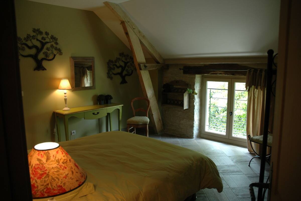 Un dormitorio con cama, escritorio, silla y ventana con vista a follaje.