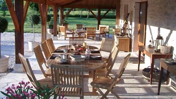 An outdoor patio with a wooden table and chairs, surrounded by stone walls and potted plants. - Au Picatal (Meyronne)