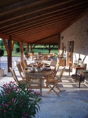 An outdoor patio with a wooden table and chairs, surrounded by stone walls and potted plants. - Au Picatal (Meyronne)