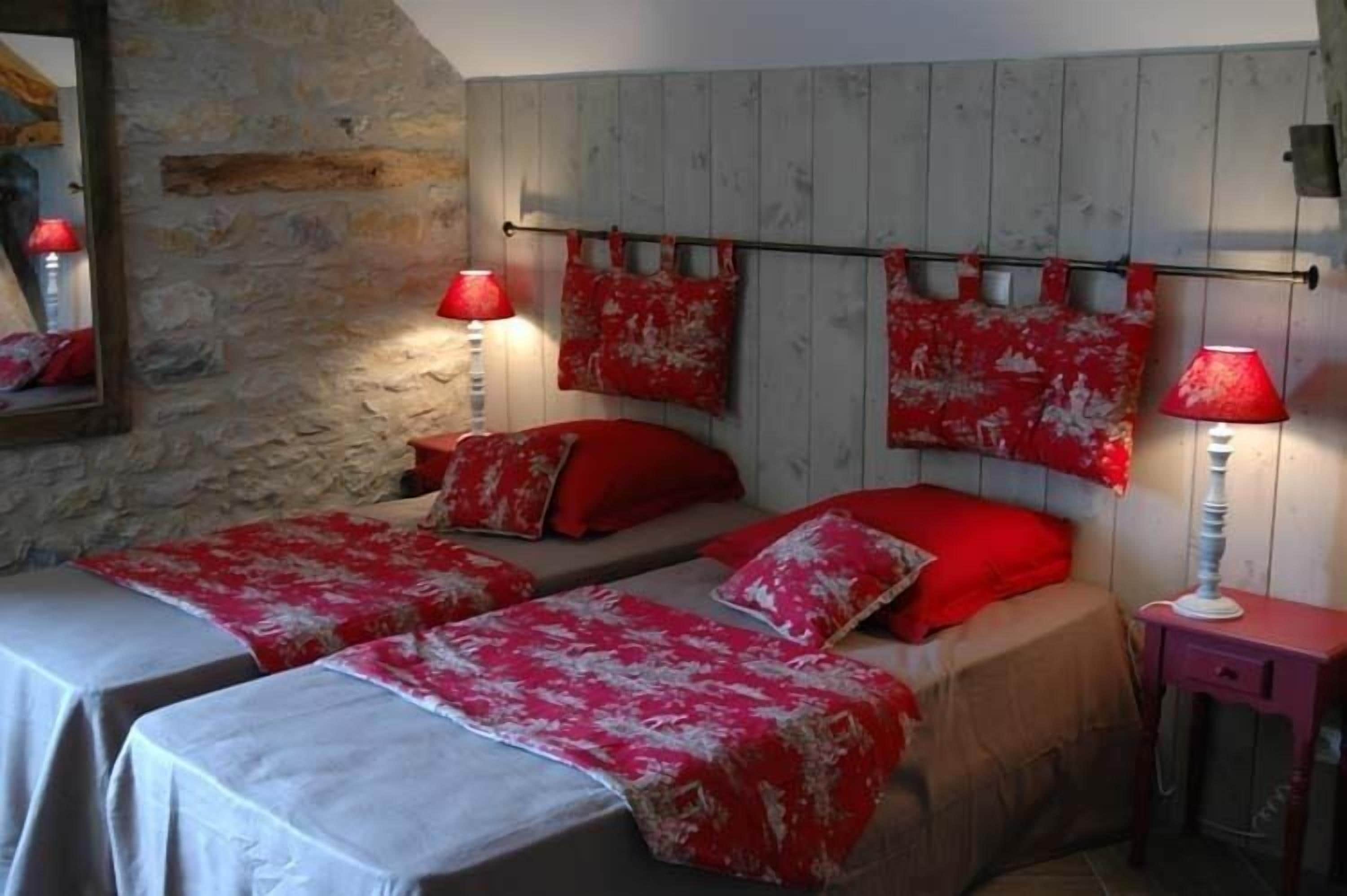 A room with two beds, each with red and white bedding, a stone wall, and a wooden headboard.