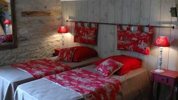 A room with two beds, each with red and white bedding, a stone wall, and a wooden headboard.