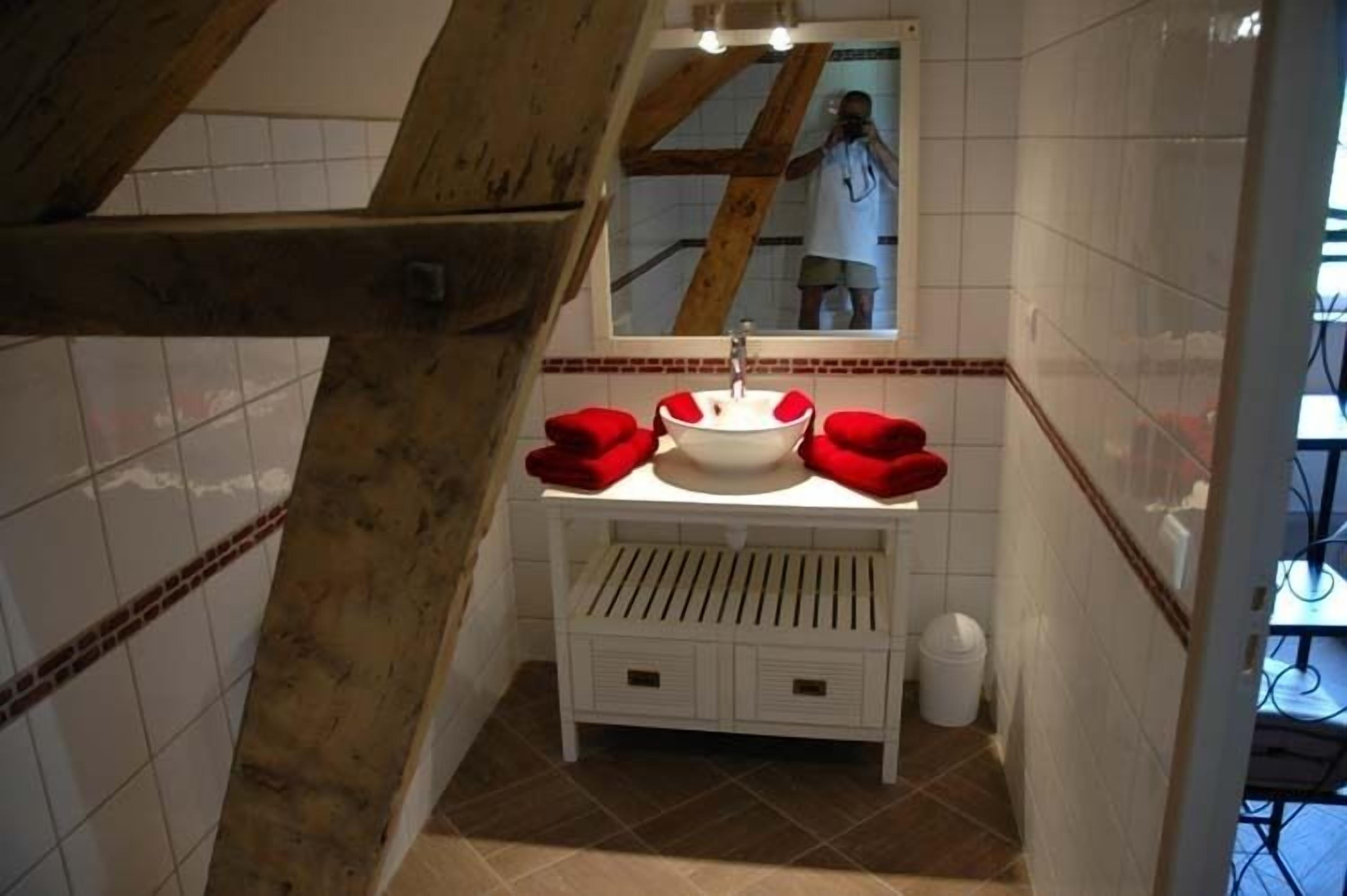 Un bagno con un mobile lavabo bianco, asciugamani rossi, uno specchio e un pavimento piastrellato.