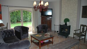 A living room with a fireplace, a television, and a large window with a view of greenery. - Au Picatal (Meyronne)