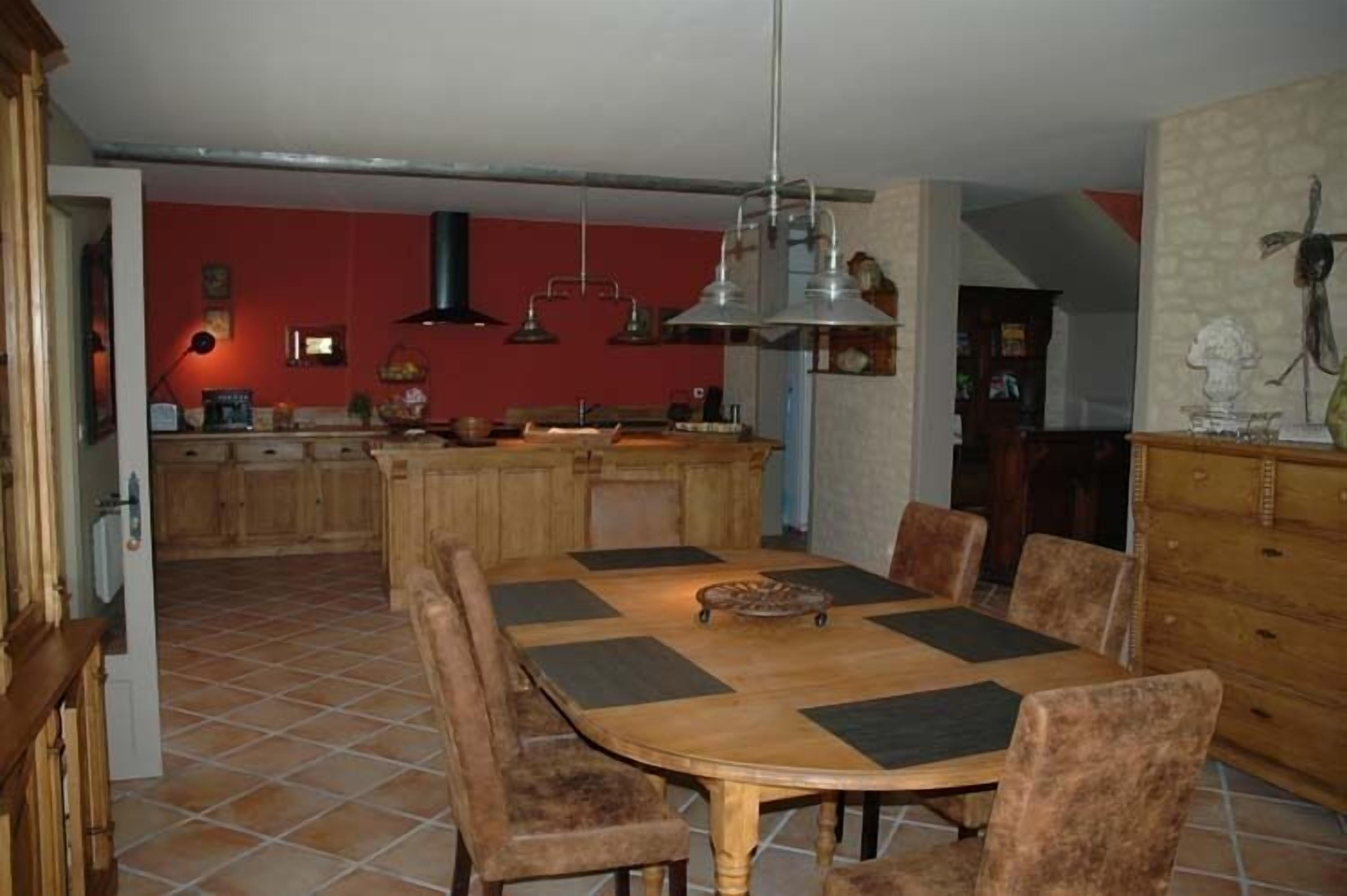Ein Essbereich mit Holztisch und -stühlen, im Hintergrund eine Küche und eine rote Wand.