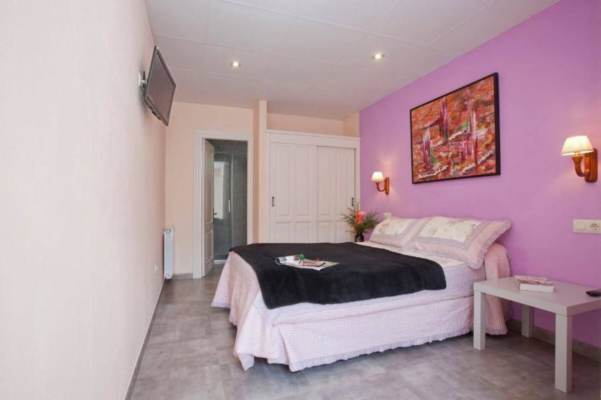 A bedroom with a bed, a bedside table, a wall-mounted TV, and a painting.