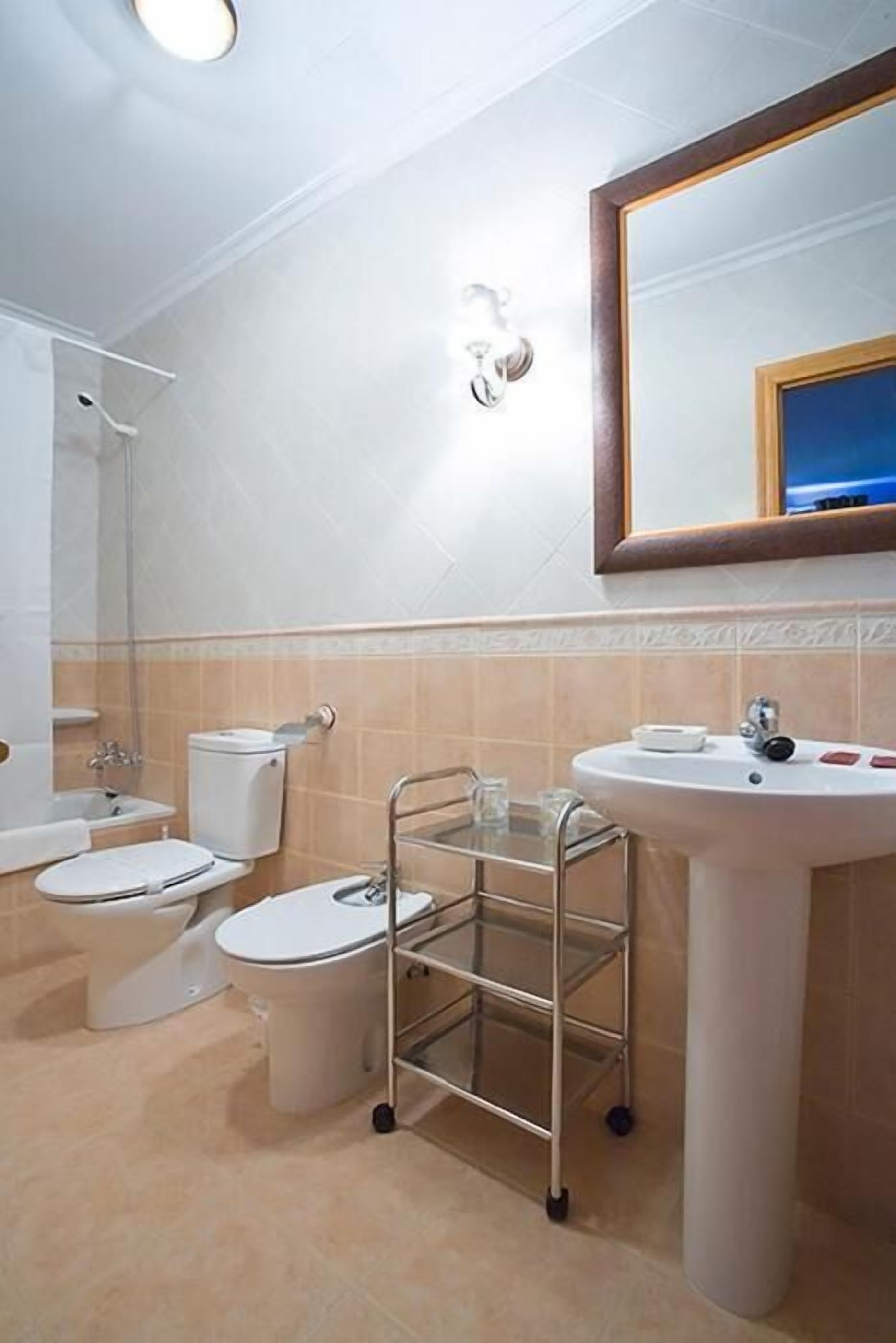 A bathroom with a sink, two toilets, a shower, and a mirror.