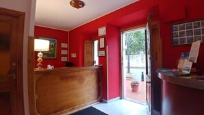 A reception area with a wooden reception desk, a red wall, and a door leading outside. - Hotel Alvaro (Cudillero)