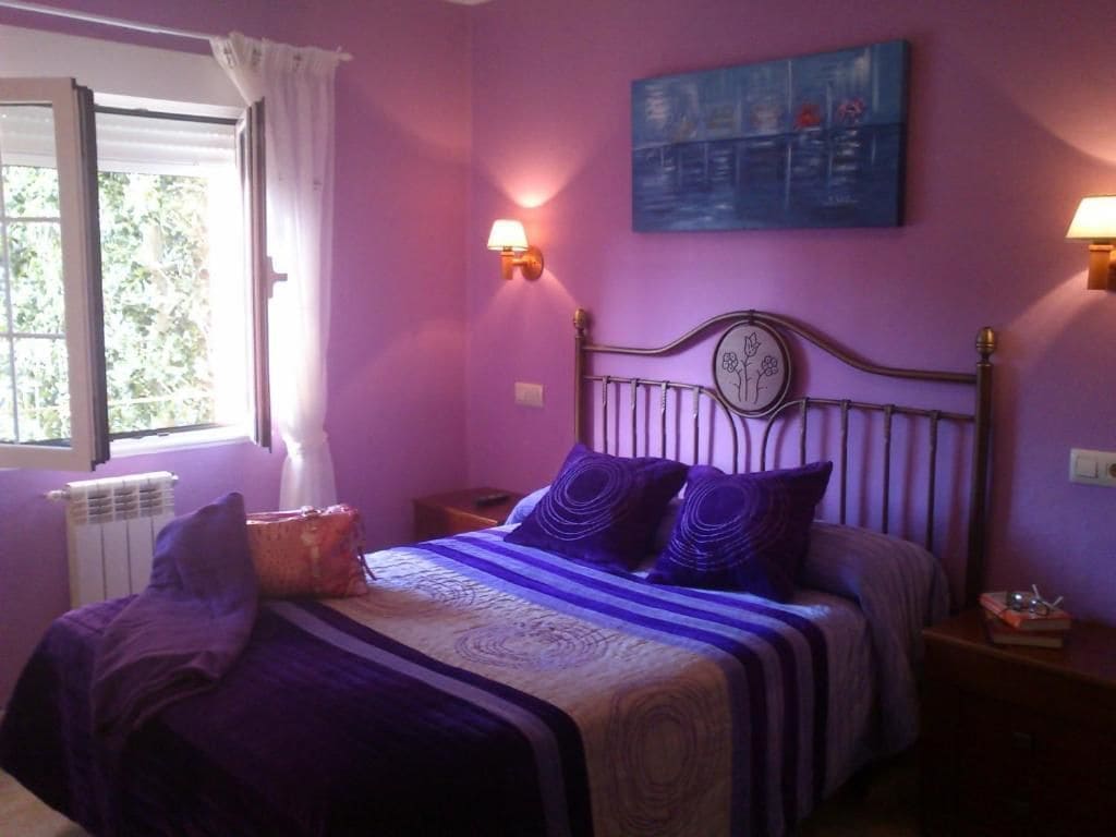 A bedroom with a bed, two bedside tables, a window with curtains, and a wall-mounted painting.