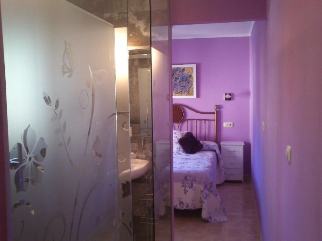 A bedroom with a bed, a nightstand, a wall-mounted painting, and a bathroom with a sink and mirror.
