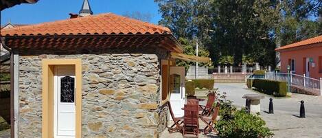 Un edificio de piedra con tejado de baldosas, una puerta y un pequeño patio con mesa y sillas.