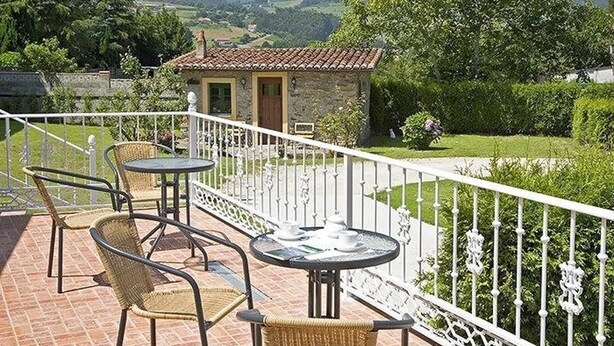 A terrace with wicker chairs and a table, a small stone building, and a white fence. - Hotel Alvaro (Cudillero)