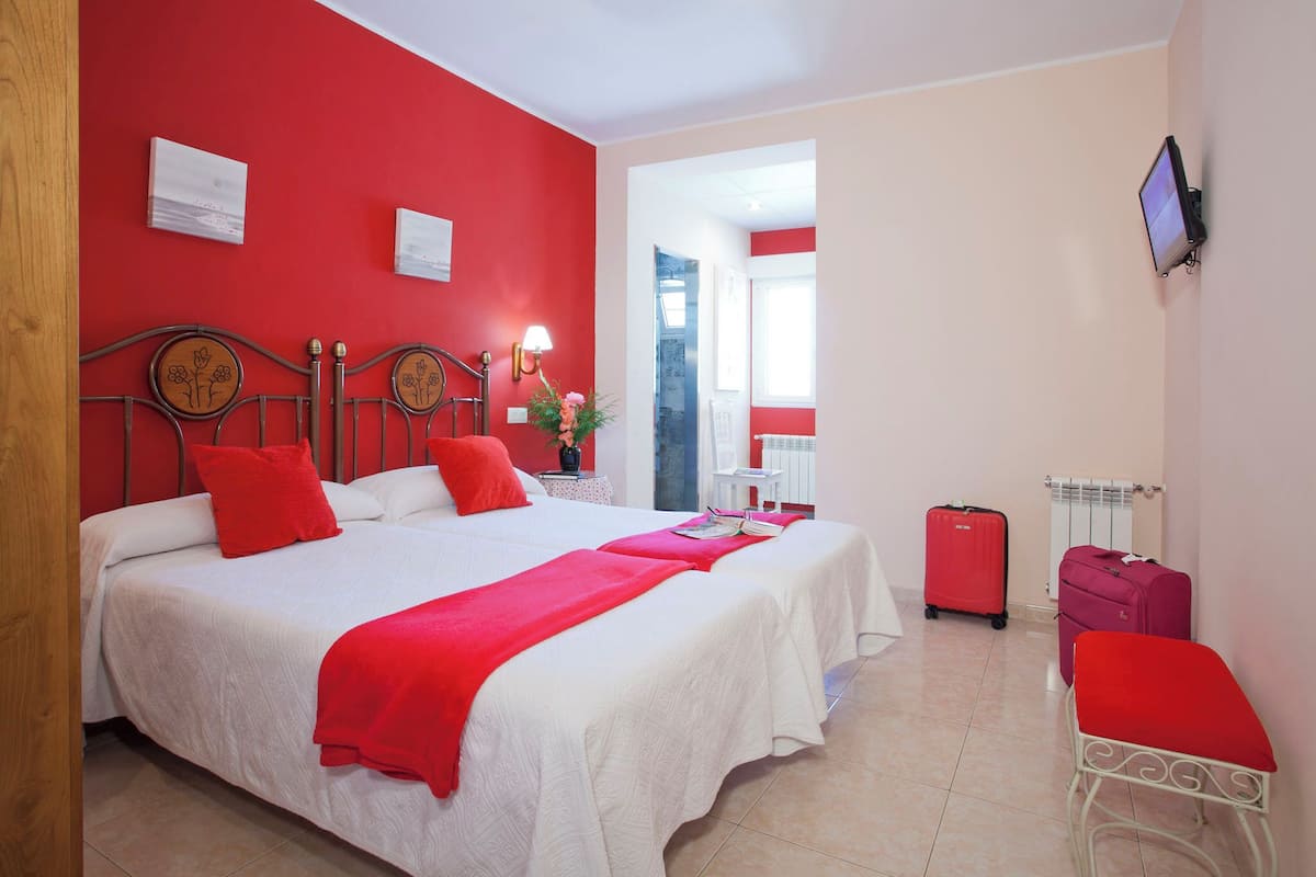 A hotel room with a large bed, red accents, a TV, and a suitcase.