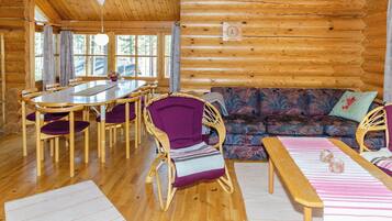 A log cabin interior with a dining table, chairs, a sofa, and a clock on the wall.