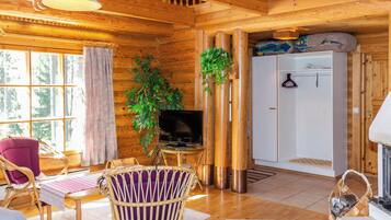 A wooden cabin interior with a television, wicker furniture, a fireplace, and a large window.