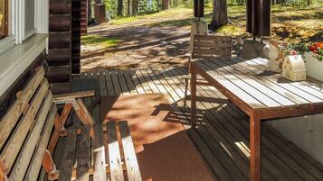 A wooden deck with a bench and table, surrounded by a forest.