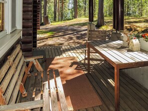Una terraza de madera con un banco y una mesa, rodeada de un bosque.