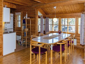 A wooden cabin interior with a dining table, chairs, a kitchen area, and large windows. - Honkakoli 9/1 by Interhome (Lieksa)
