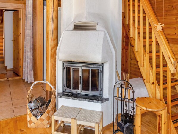 A wooden interior with a fireplace, a wooden bench, a basket, and a metal rack. - Honkakoli 9/1 by Interhome (Lieksa)