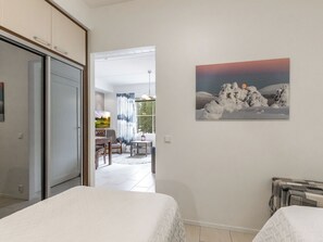 A hotel room with a bed, a painting of a snowy landscape, and a view of the dining area.