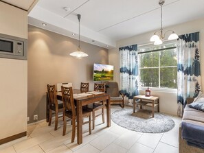 A modern living room with a dining area, a TV mounted on the wall, and a window with curtains.