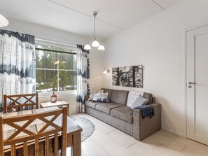 A room with a sofa, a dining table with chairs, a window with curtains, a lamp, and a door.