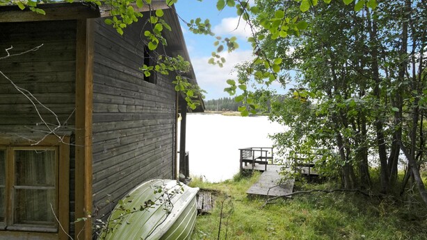 Un rustico chalet con un molo che si protende su un lago, immerso nel verde.