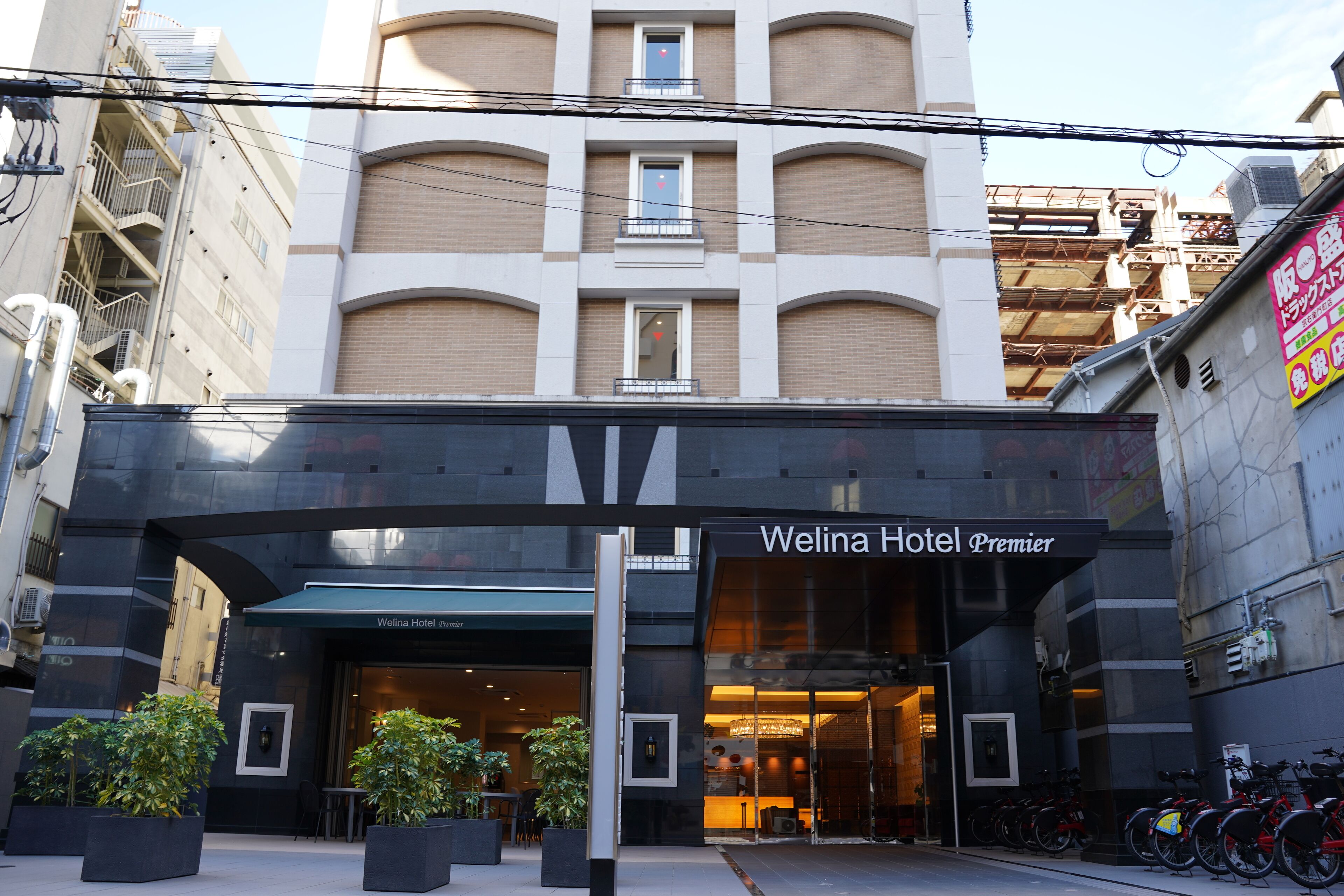 The Welina Hotel Premier entrance with a modern facade, large windows, and a bike parking area.