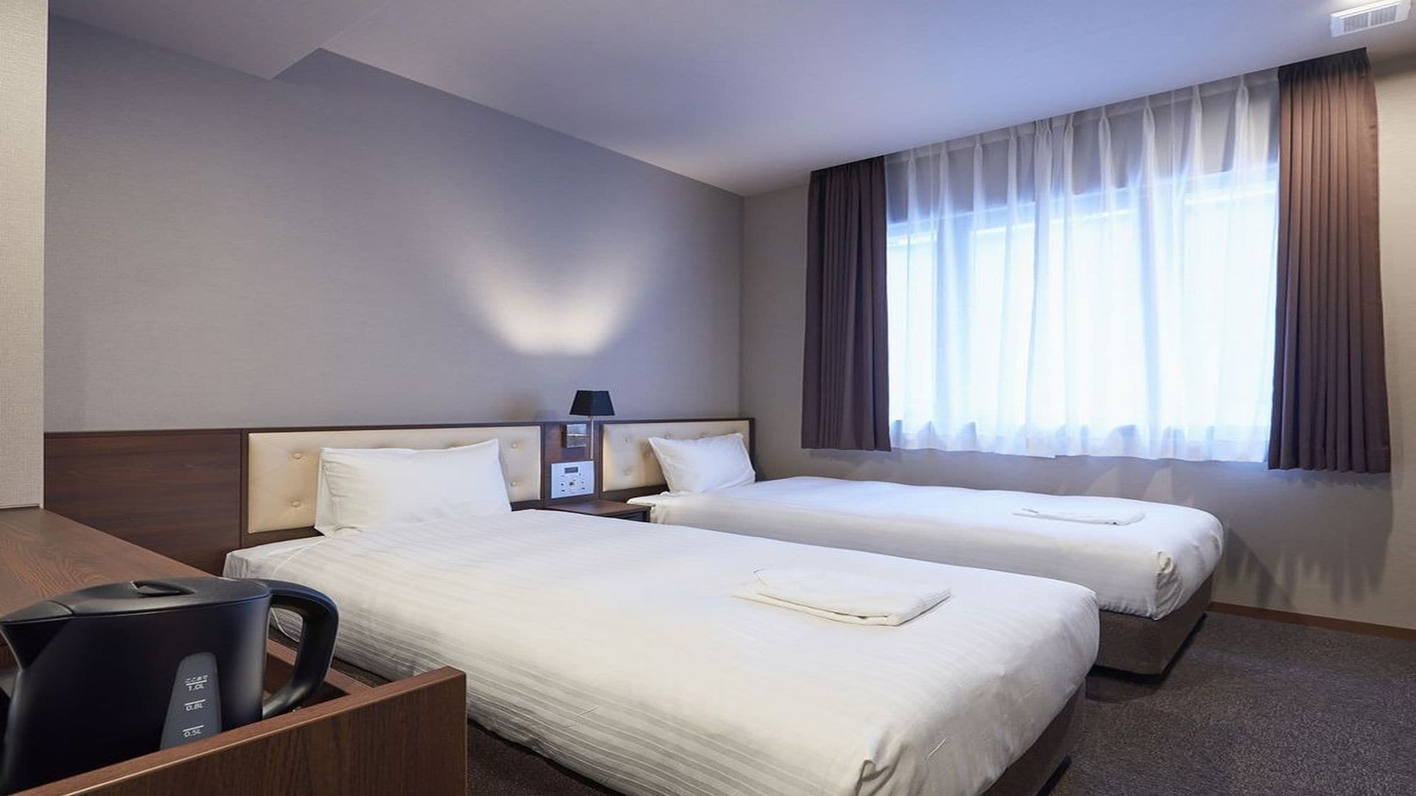 Una habitación de hotel con dos camas, un escritorio, una silla y una ventana con cortinas.