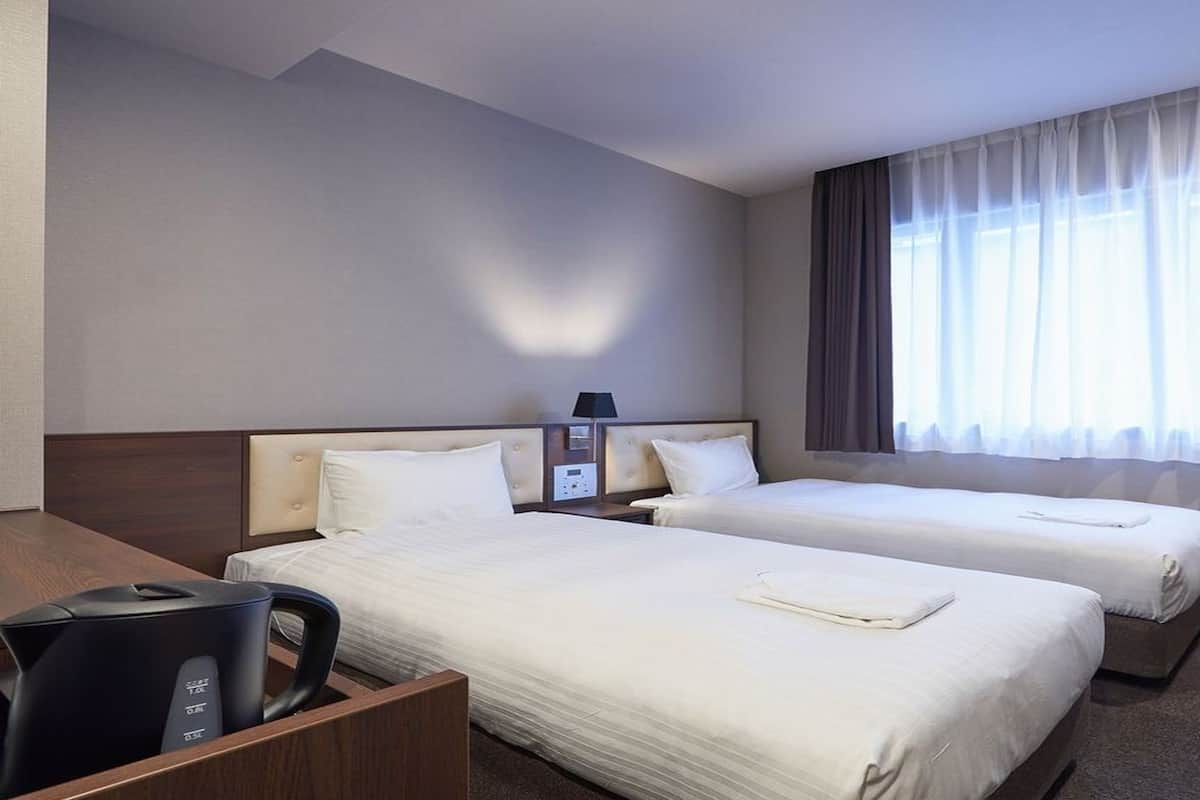 Ein Hotelzimmer mit zwei Betten, einem Schreibtisch, einem Stuhl und einem Fenster mit Vorhängen.