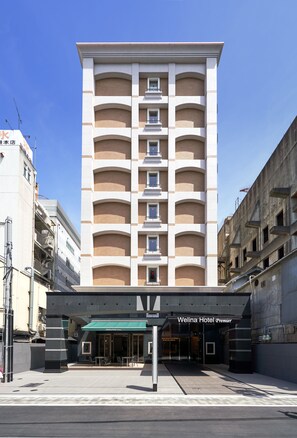 Un hôtel à la façade moderne, doté de nombreux balcons et d’une entrée imposante surmontée d’un auvent vert.