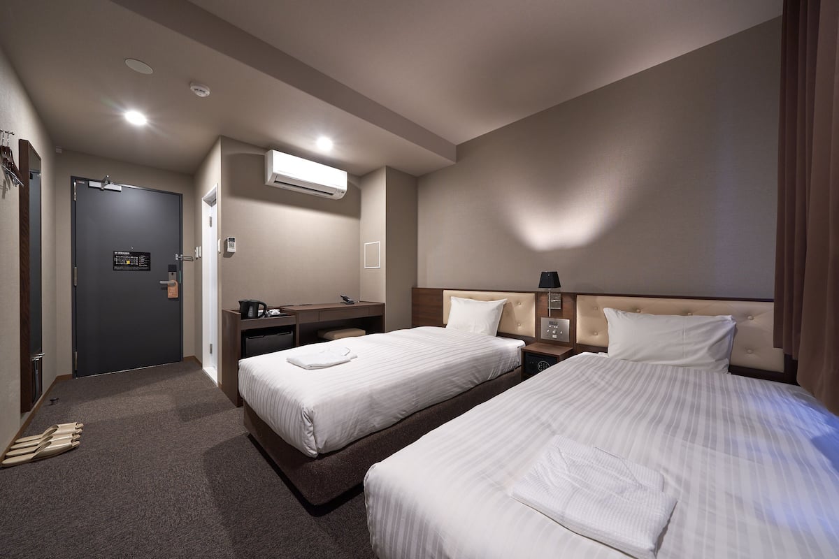 Ein Hotelzimmer mit zwei Betten, einem Schreibtisch, einem Stuhl, einem Kleiderschrank und einer Klimaanlage.