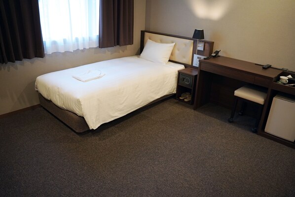 Une chambre d’hôtel avec un lit simple, un bureau, une chaise et un petit placard.