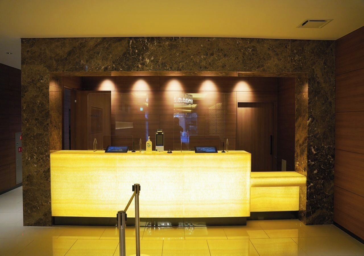 A reception desk with a marble wall backdrop, a digital screen, and a small seating area.
