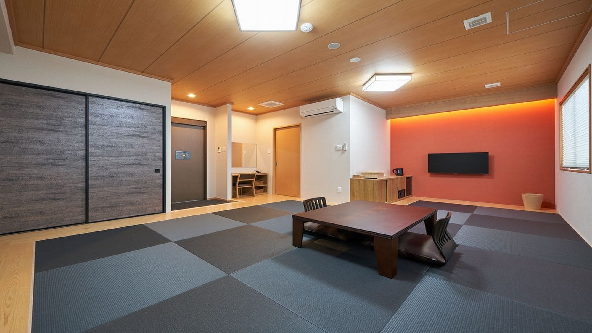 Una habitación con piso de madera, una mesa, sillas, un televisor y un equipo de aire acondicionado.