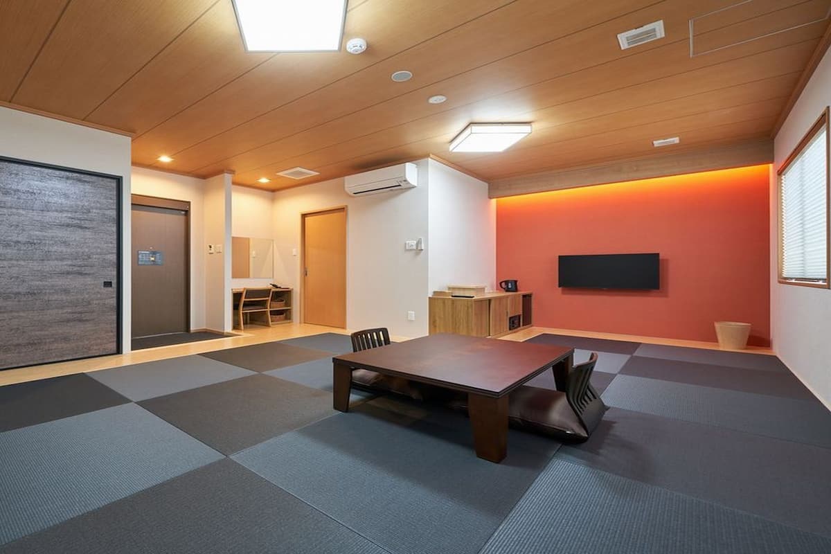 Ein Zimmer mit Holzboden, einem Tisch, Stühlen, einem Fernseher und einer Klimaanlage.