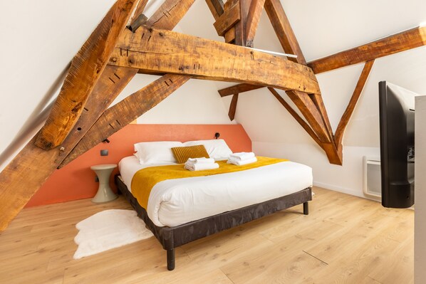 Un dormitorio con cama, vigas de madera, pared blanca y televisor.