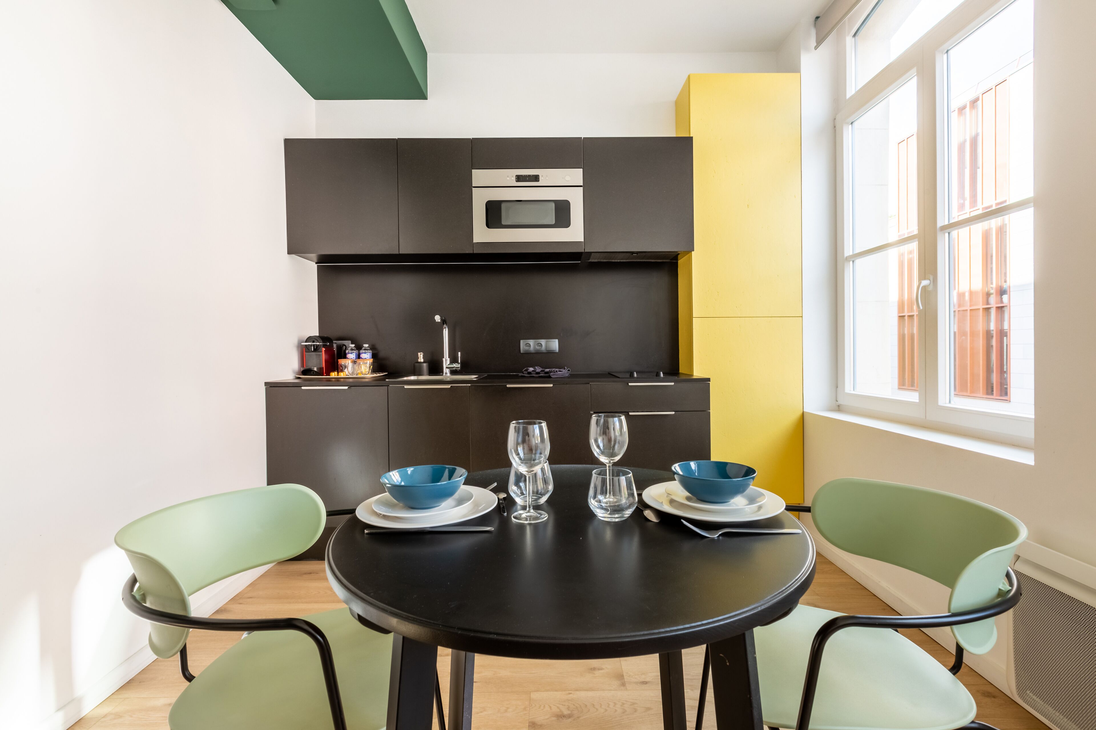 Una cocina moderna con armarios oscuros, un microondas y un lavabo. Hay una mesa de comedor con sillas y dos cuencos azules.