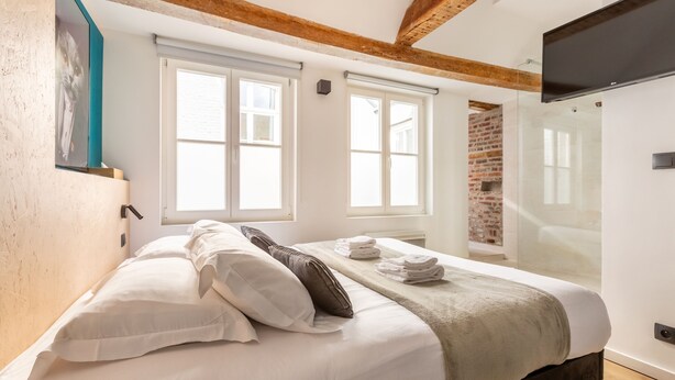 A bedroom with a bed, pillows, a blanket, and a TV mounted on the wall. - Au Chat Qui Dort Lille - Magasin  (Lille)